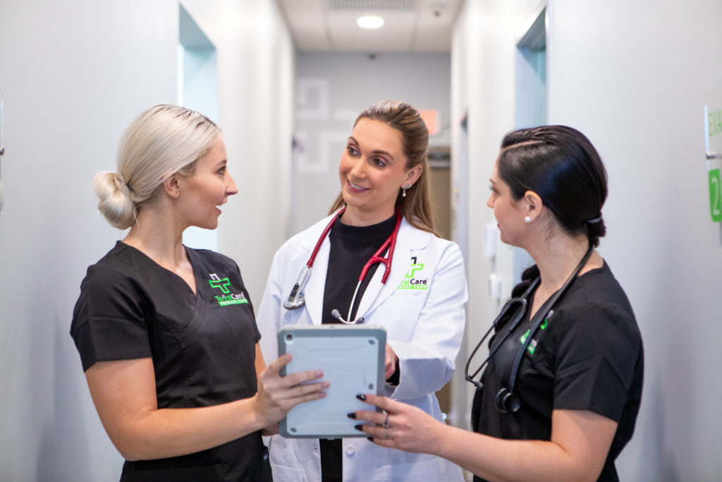 Three Total Health Primary Care staff review a patient chart on a tablet in a clinic hallway.